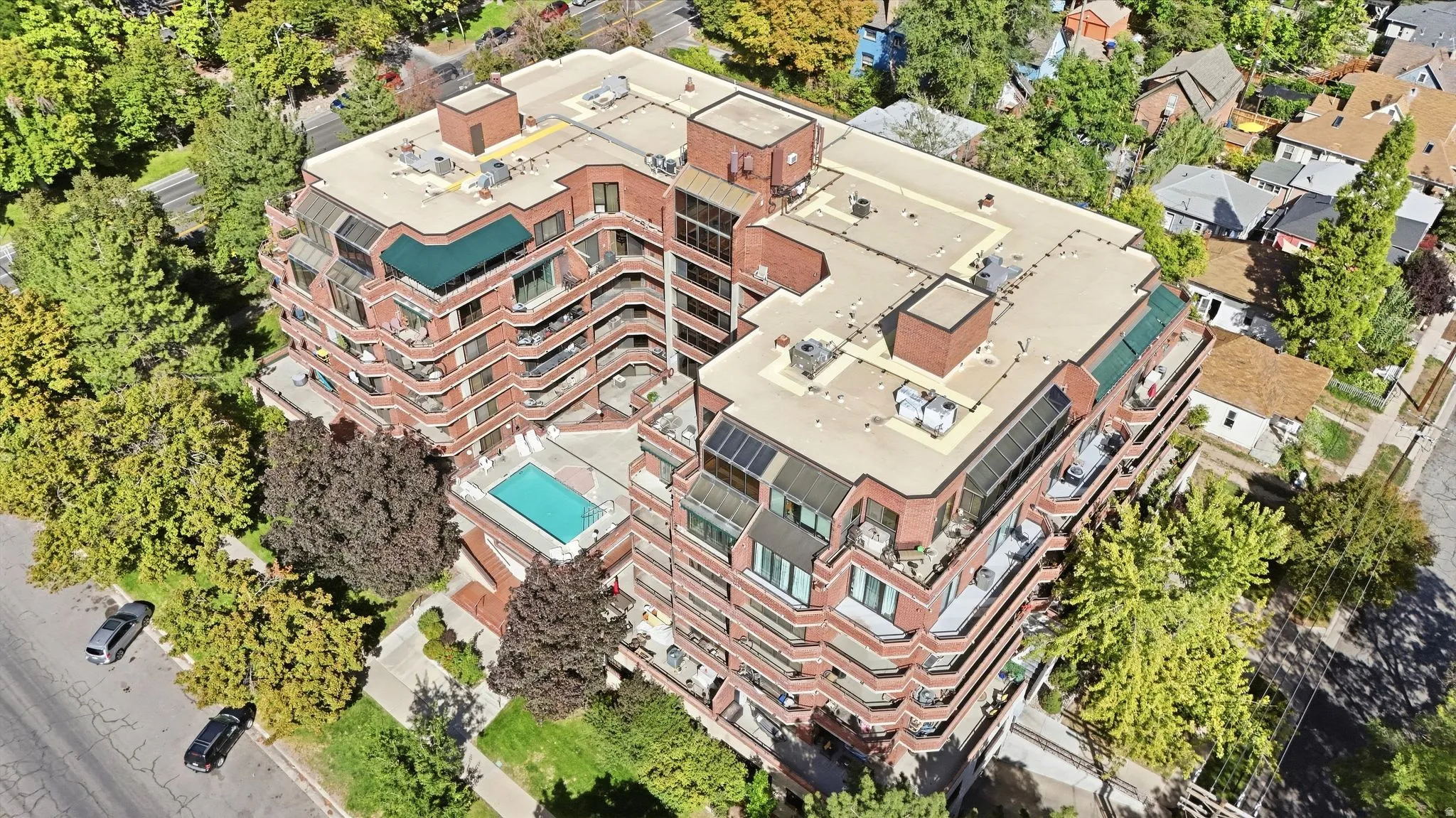 Multi-story brick facade building featuring multiple private balconies, a rooftop pool, and surrounding mature landscaping