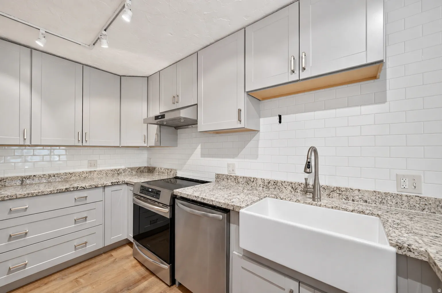 Kitchen featuring light gray cabinetry, speckled countertops, a white subway tile backsplash, stainless steel appliances, and a white farmhouse sink