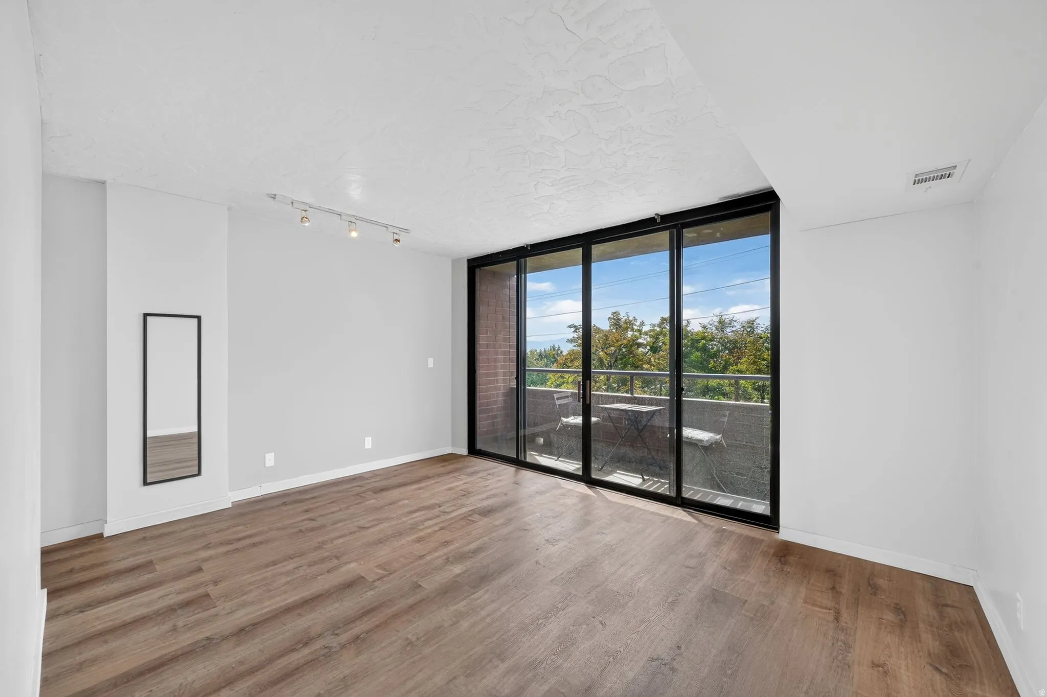 Wood-finish flooring, track lighting, and a full-height sliding glass door leading to a balcony