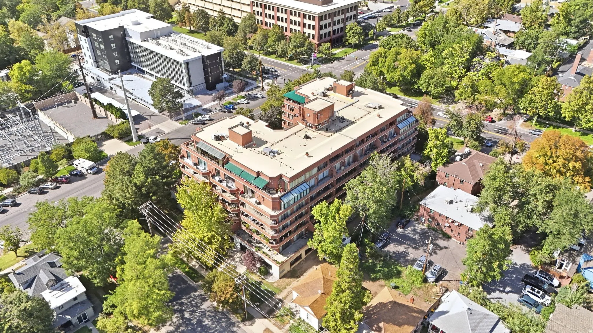 Mid-rise building featuring multiple levels of balconies, a flat roof, and surrounding mature trees
