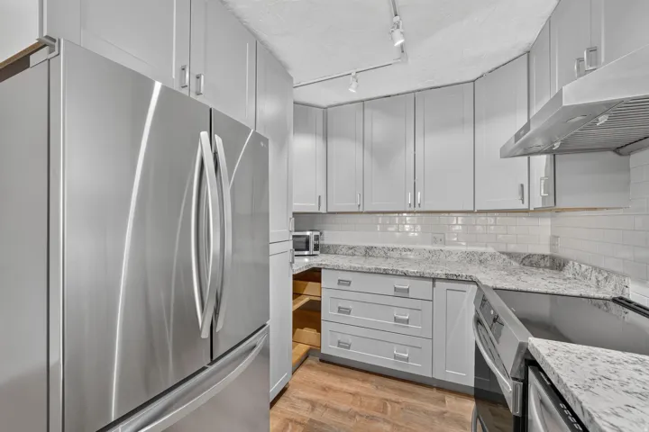 Stainless steel refrigerator, light gray cabinetry with brushed nickel hardware, white subway tile backsplash, speckled countertops, and wood-finish flooring