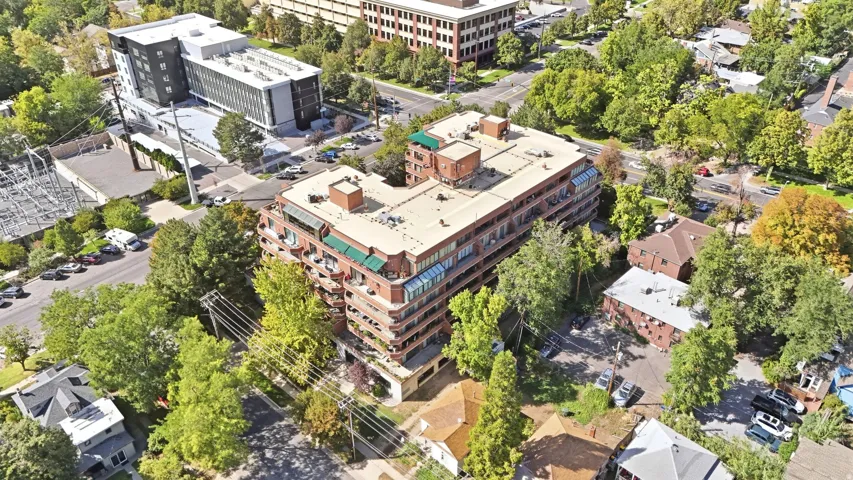 Mid-rise building featuring multiple levels of balconies, a flat roof, and surrounding mature trees