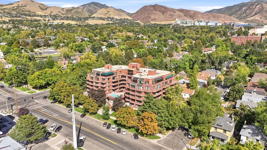 Multi-story brick building featuring balconies, flat roof with a green canopy, and surrounding mature trees