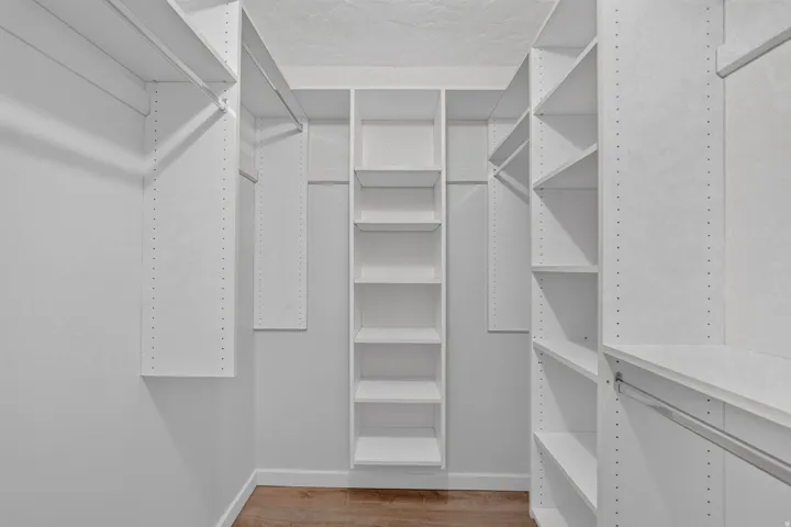 Built-in shelving, multiple hanging rods, and wood-finish flooring