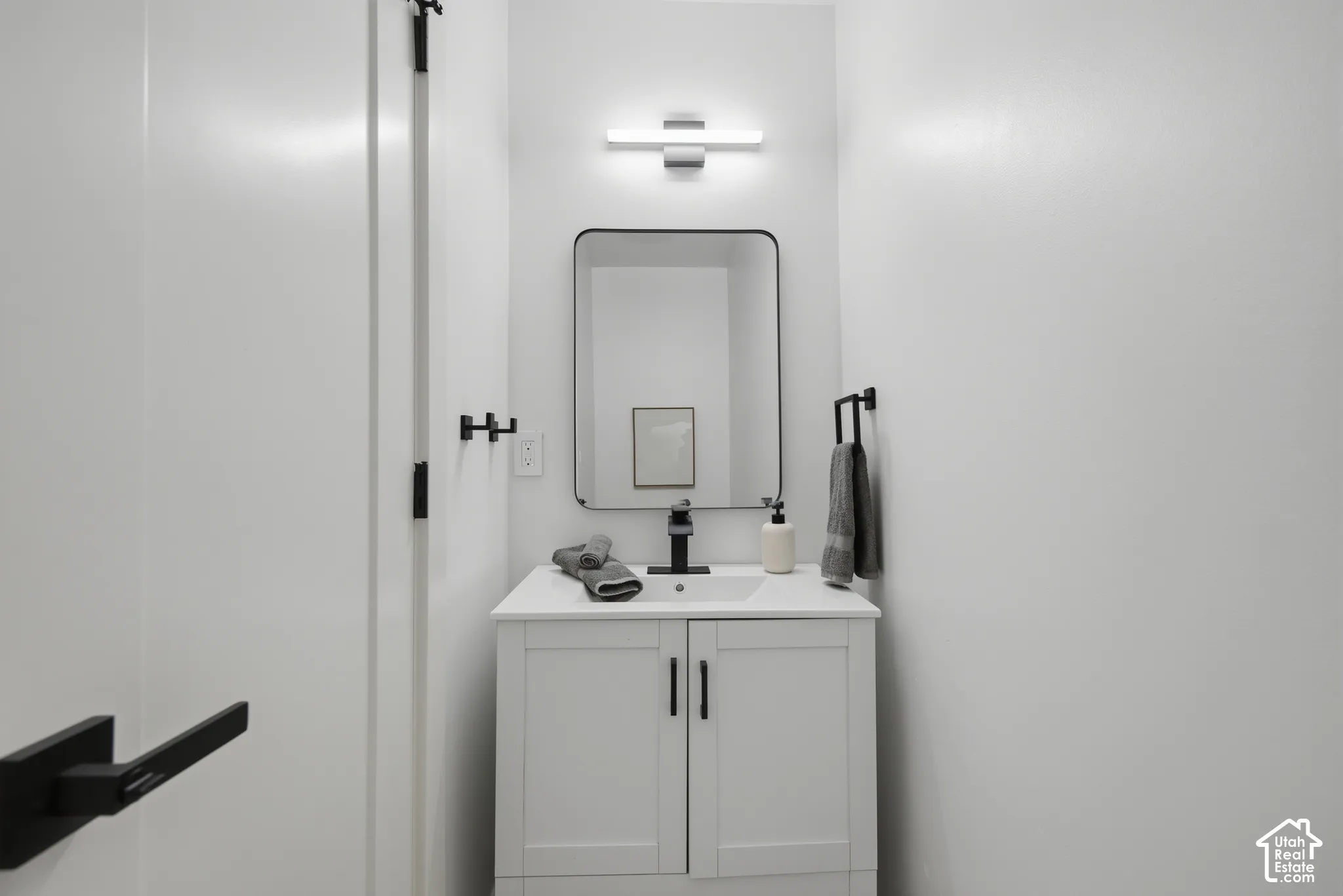 White vanity with integrated sink, black hardware, contemporary rectangular mirror, and modern wall-mounted light fixture