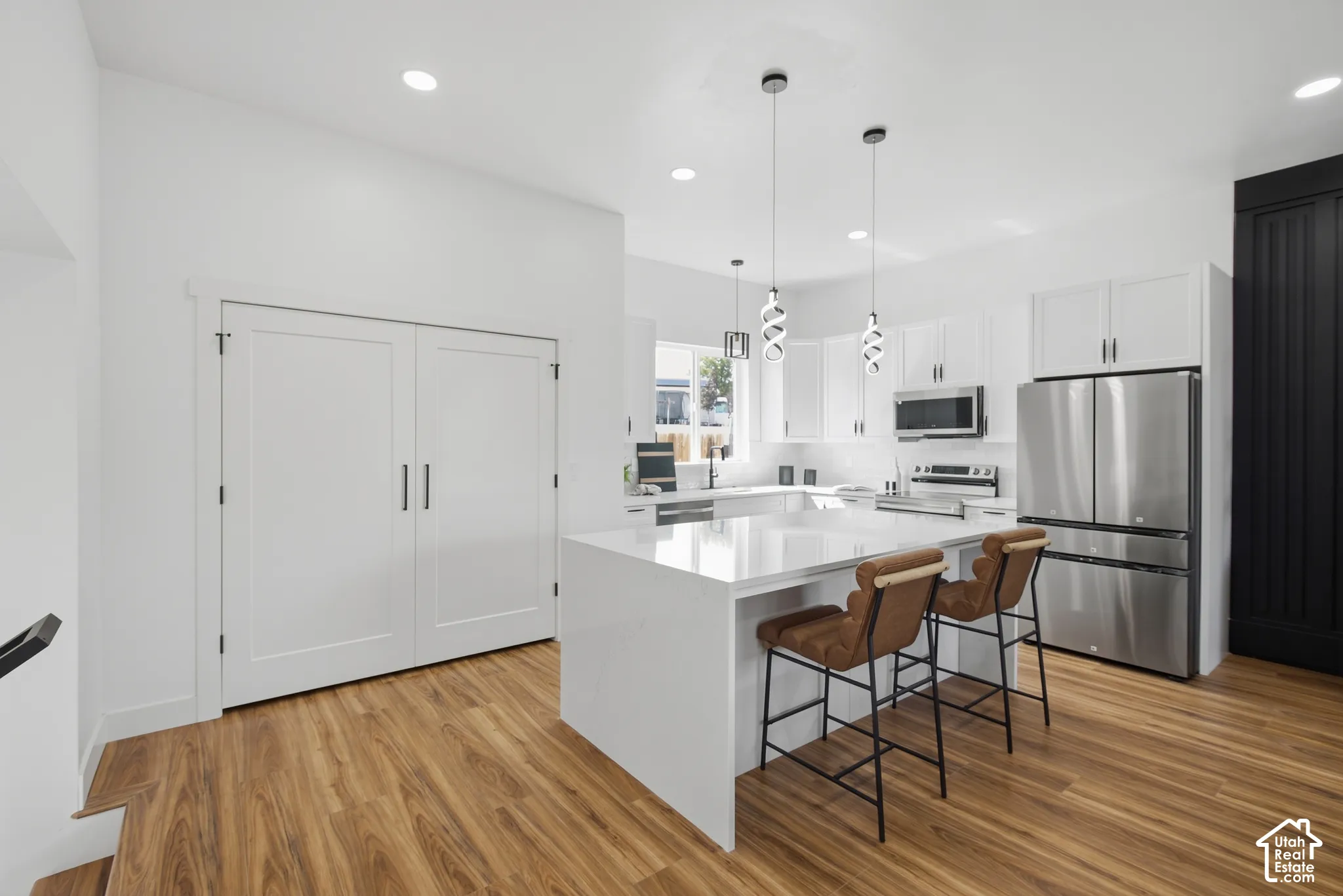 Modern kitchen featuring white cabinetry, stainless steel appliances, a center island with a white countertop, and wood-finish flooring