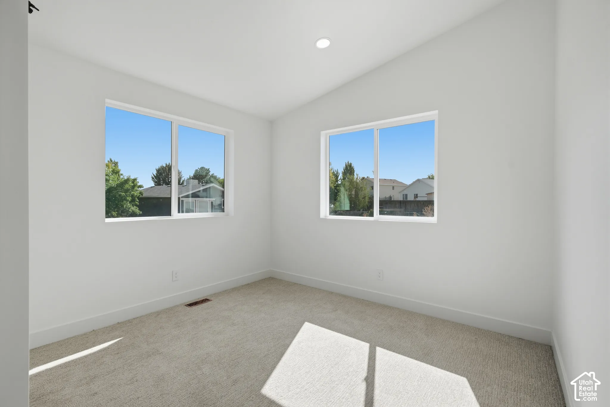 Neutral wall paint, recessed lighting, two windows, carpet flooring, and a vaulted ceiling