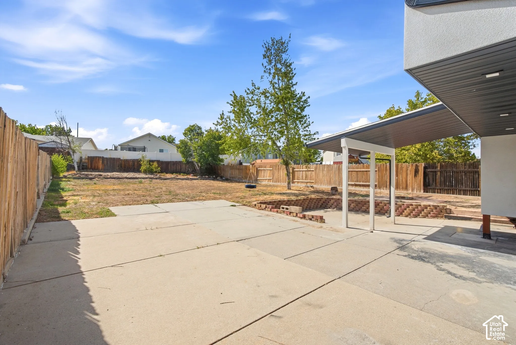 Expansive backyard with concrete patio, wood fencing, and a covered patio area