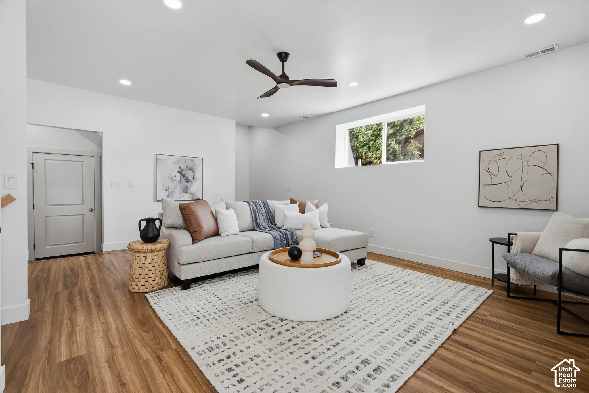 Recessed lighting illuminates the open living space, featuring wood-finish flooring and a ceiling fan