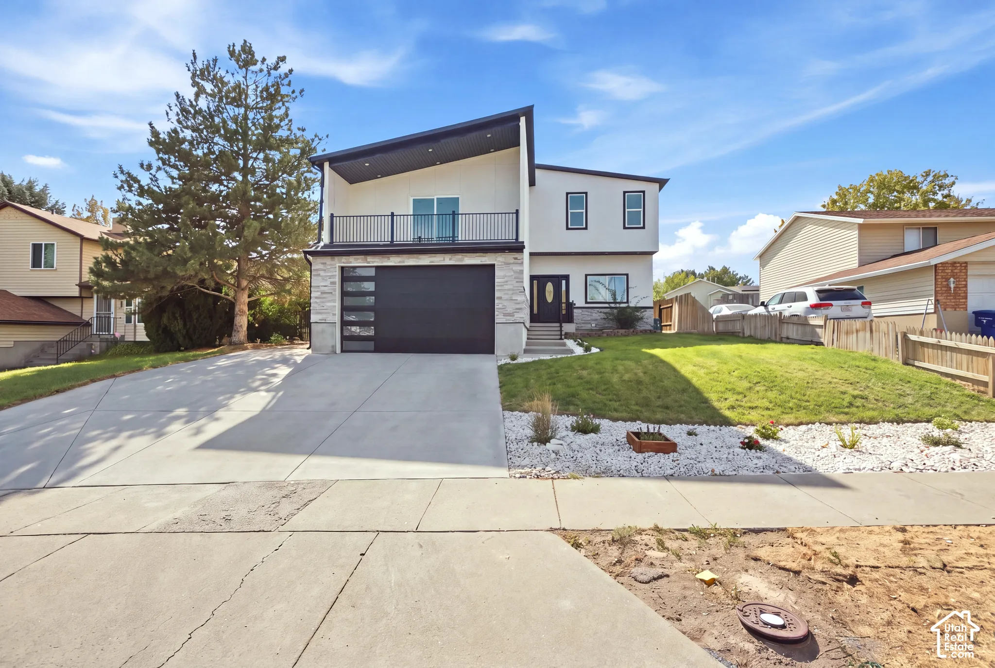 Contemporary exterior design, stone veneer accents, upper-level balcony with railing, integrated garage door with opaque glass panels, and a well-maintained lawn