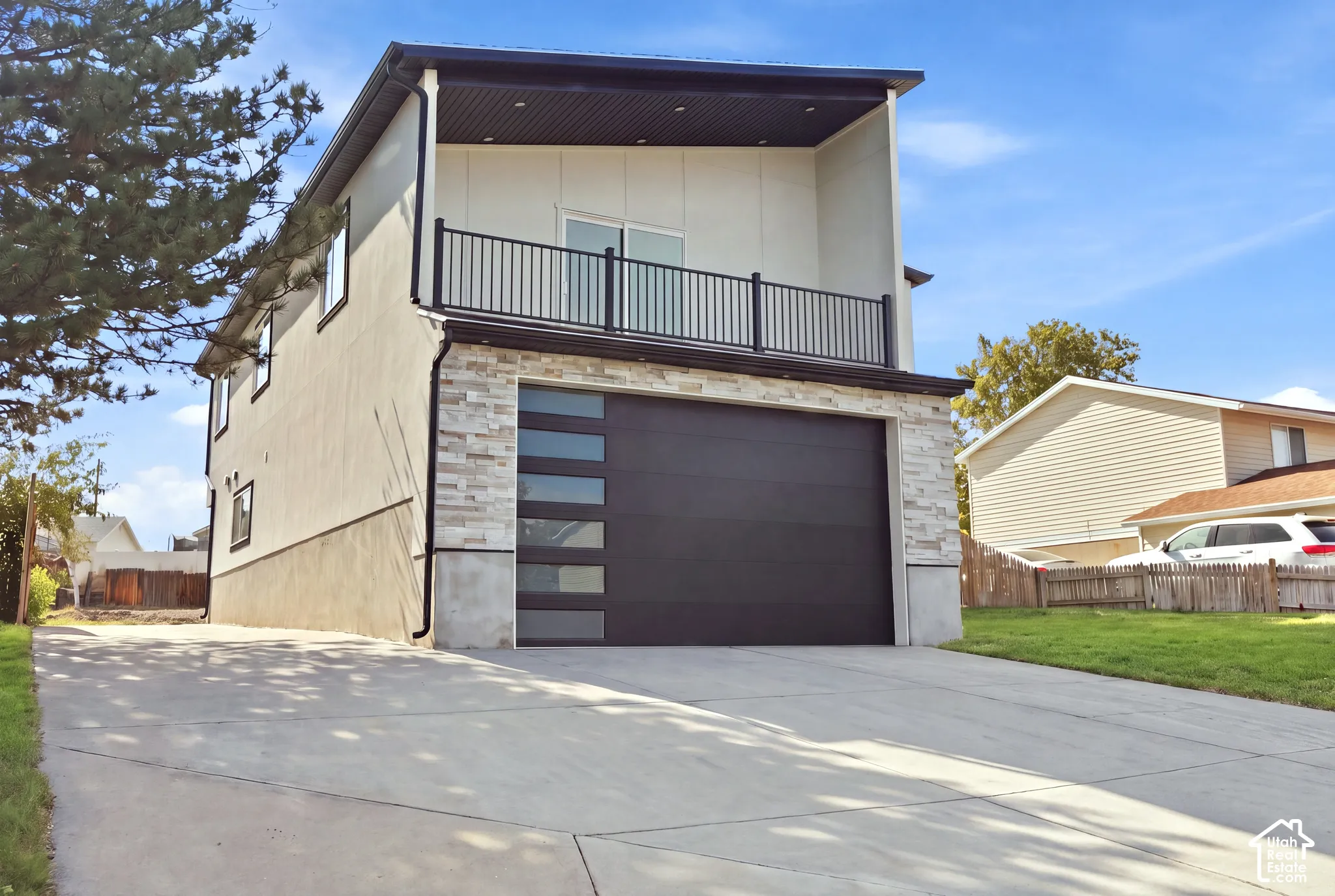 Two-story exterior with a second-level balcony, a modern garage door with frosted panels, light-toned siding, and a stone facade accent
