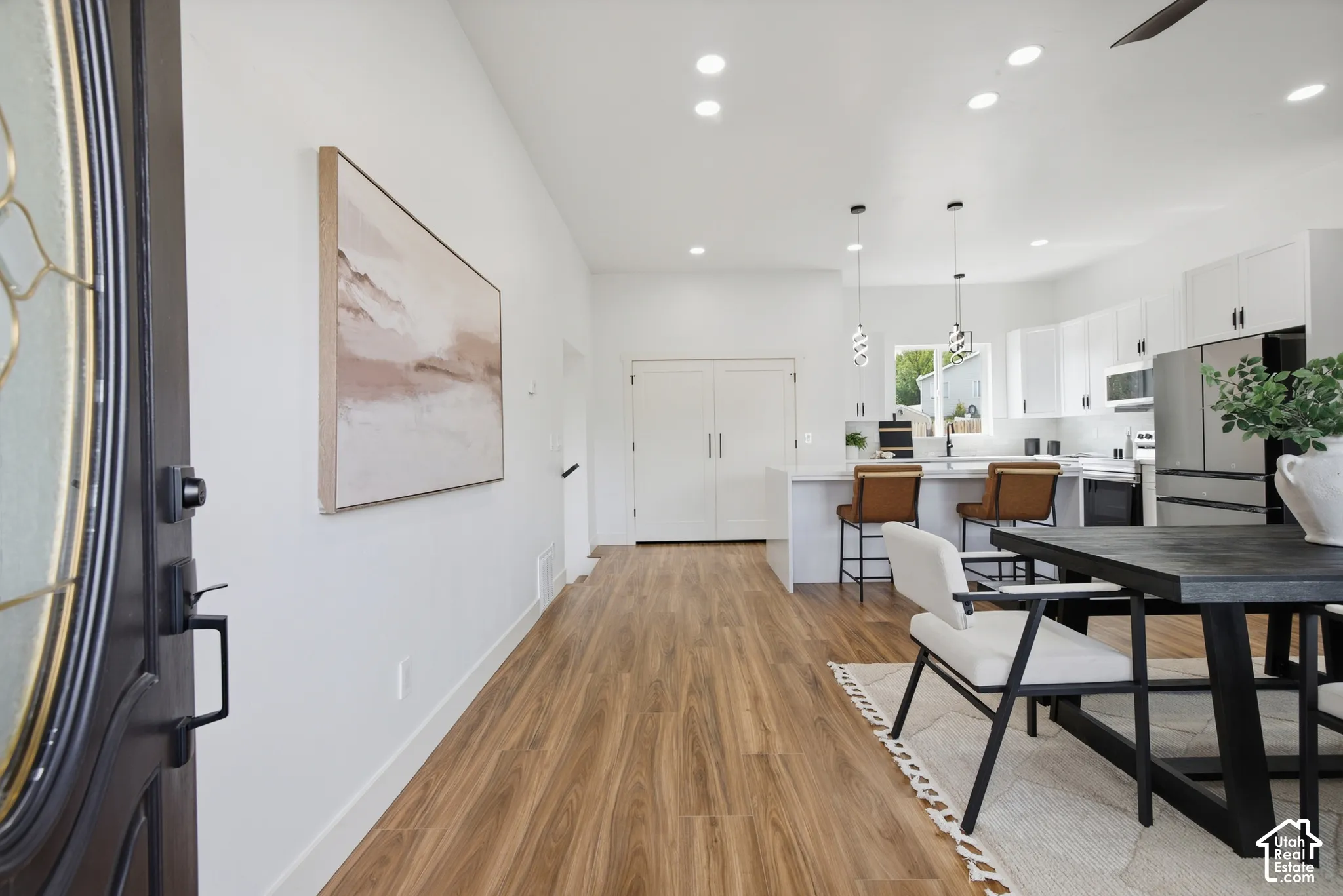 Open-concept layout featuring wood-finish flooring, recessed lighting, and a kitchen with white cabinetry and stainless steel appliances