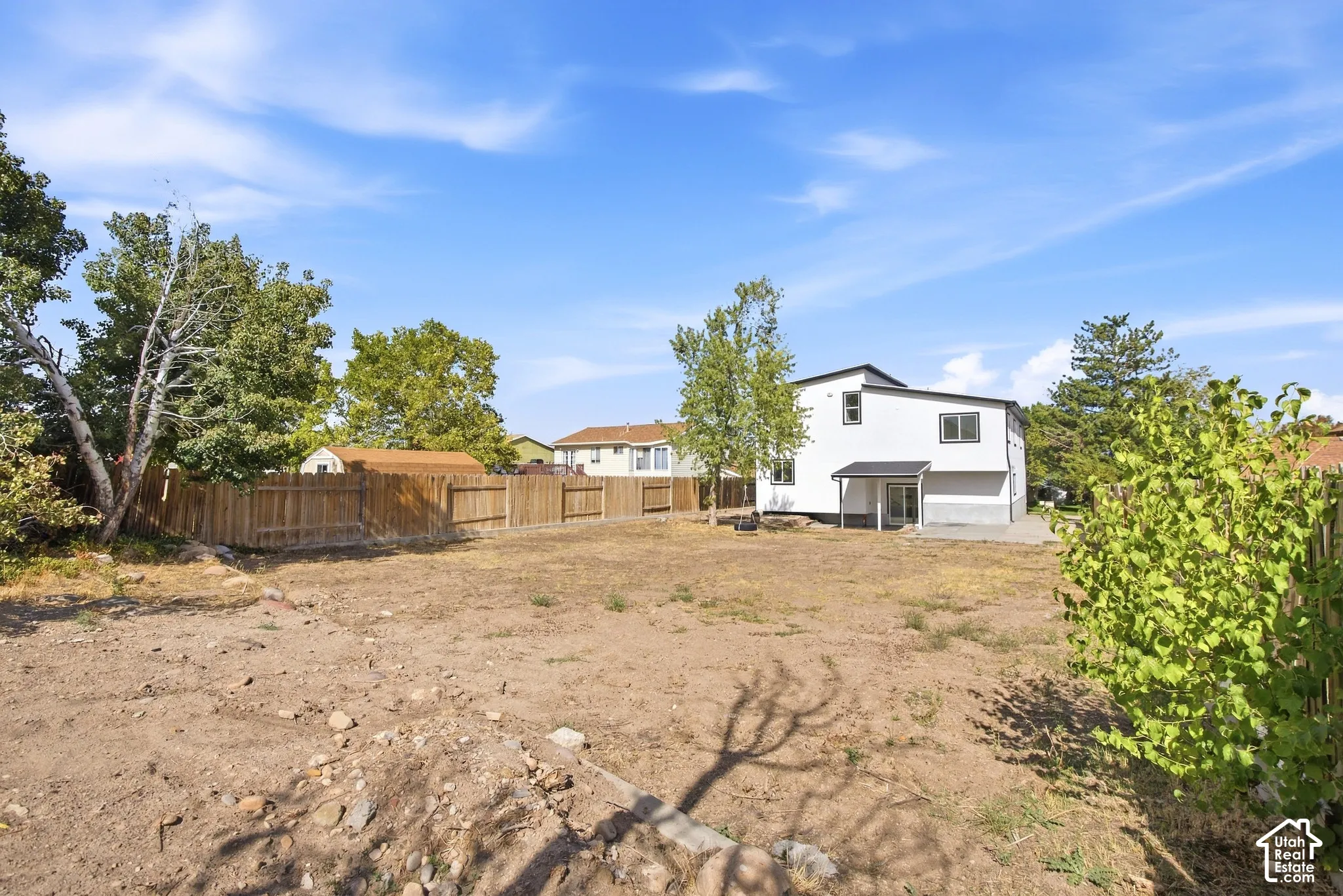 Spacious backyard with a wood privacy fence, mature trees, and a modern white exterior