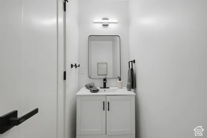 White vanity with integrated sink, black hardware, contemporary rectangular mirror, and modern wall-mounted light fixture