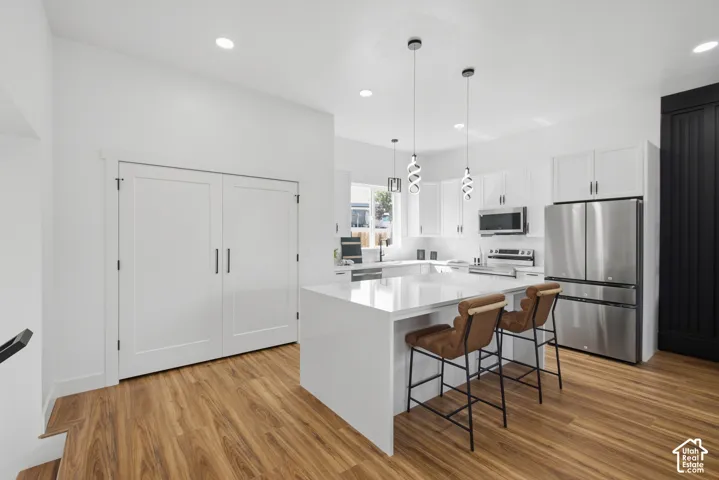 Modern kitchen featuring white cabinetry, stainless steel appliances, a center island with a white countertop, and wood-finish flooring