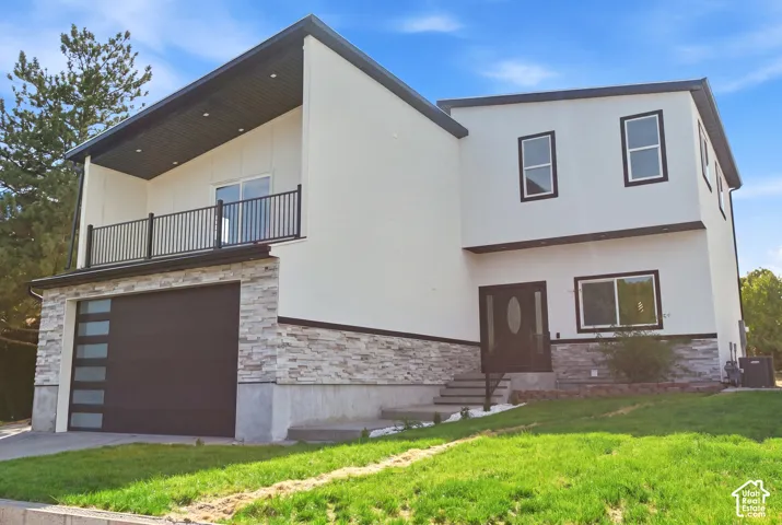 Modern exterior with white stucco siding, stacked stone accents, a dark garage door with frosted panels, a second-story balcony with dark railings, and a dark entry door with an oval glass insert
