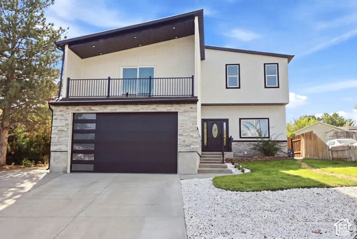 Modern exterior with stucco and stacked stone accents, featuring a contemporary garage door with frosted glass panels, a front entry with a black door and oval glass insert, and a second-story balcony with black railing