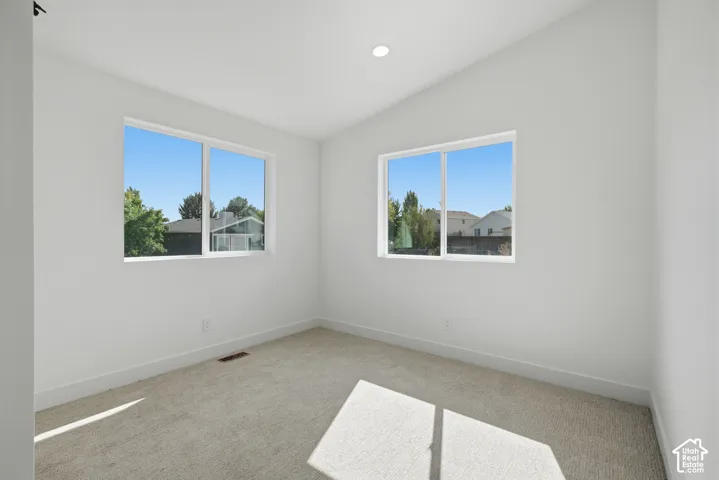 Neutral wall paint, recessed lighting, two windows, carpet flooring, and a vaulted ceiling