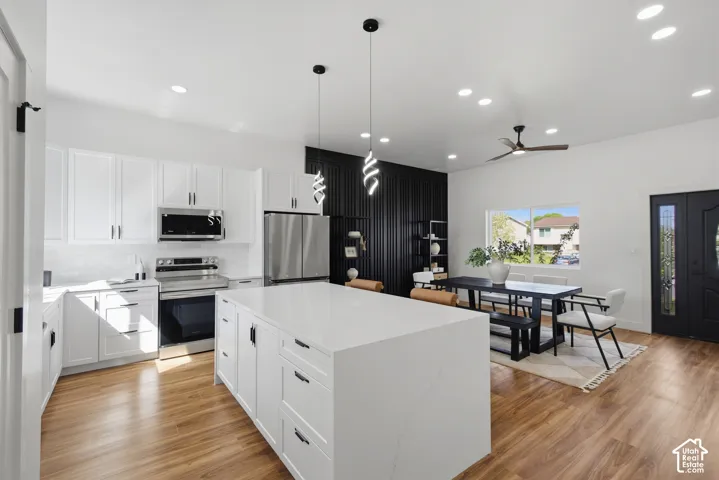 White shaker cabinetry, stainless steel appliances, wood-finish flooring, recessed lighting, and a kitchen island with a white countertop