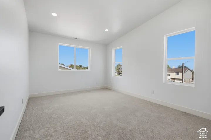 Spacious room featuring three windows, neutral-toned carpet, recessed lighting, and white walls