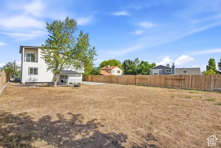 Expansive backyard featuring a wood fence, concrete patio, and mature tree