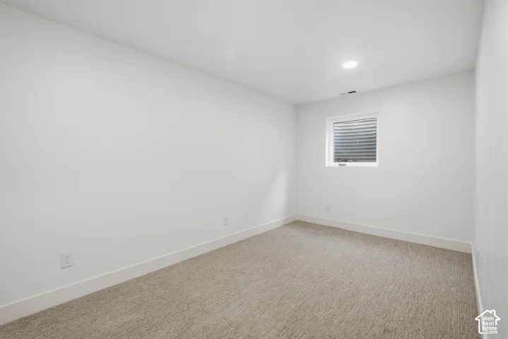 Neutral tone carpeting, recessed lighting, white walls, and a window with blinds