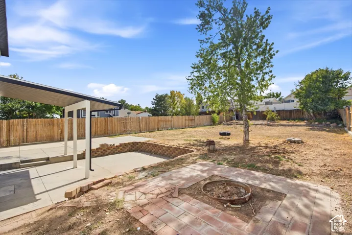 Expansive backyard featuring a covered patio, brick hardscaping, a retaining wall, and a mature tree