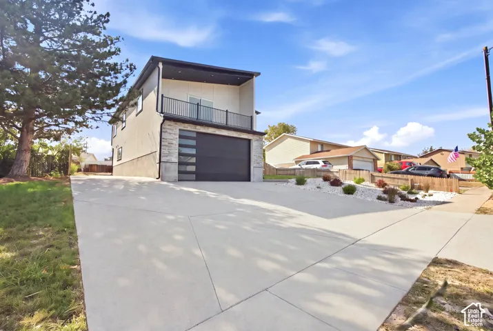 Contemporary exterior with stucco and stone veneer accents, a second-story balcony with black railing, a multi-paneled garage door, and a concrete driveway