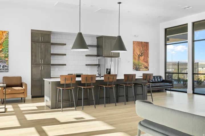 Spacious open-concept room featuring light wood-finish flooring, a kitchen island with seating, dark wood-finish cabinetry, a stainless steel refrigerator, and large windows