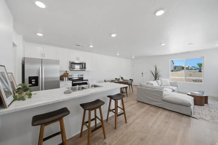 Contemporary kitchen with stainless steel appliances, white cabinetry, a large center island, and wood-finish flooring throughout