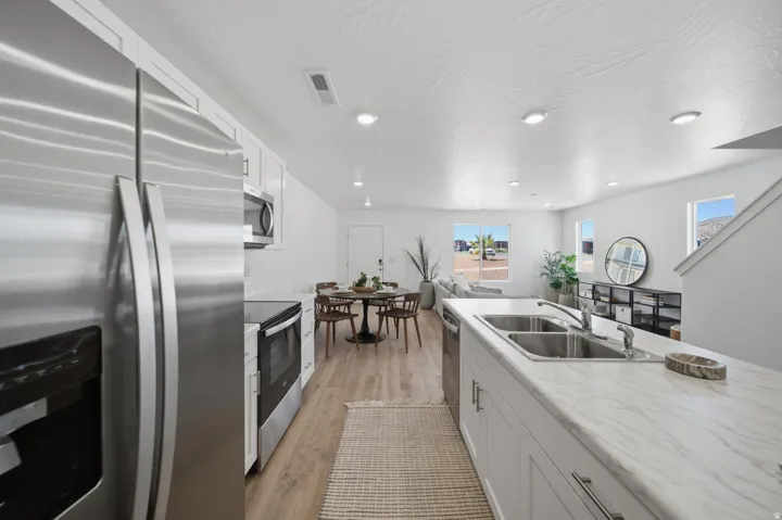 Kitchen with stainless steel appliances, white cabinetry, and wood-finish flooring