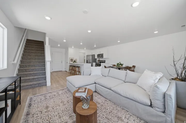 Open-concept living space with wood-finish flooring, recessed lighting, and a white kitchen featuring stainless steel appliances