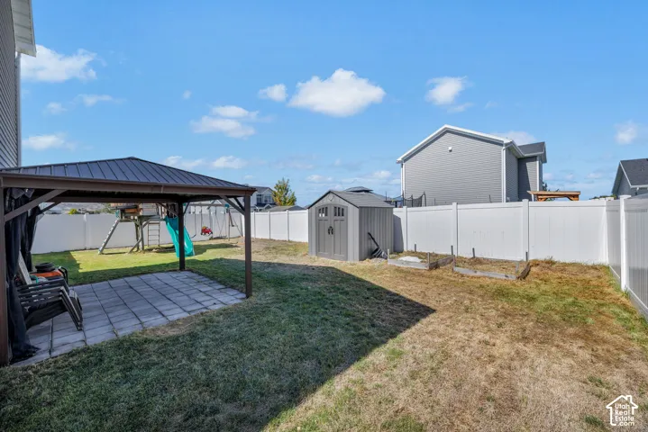 Expansive backyard featuring a covered patio, privacy fencing, storage shed, and raised garden beds