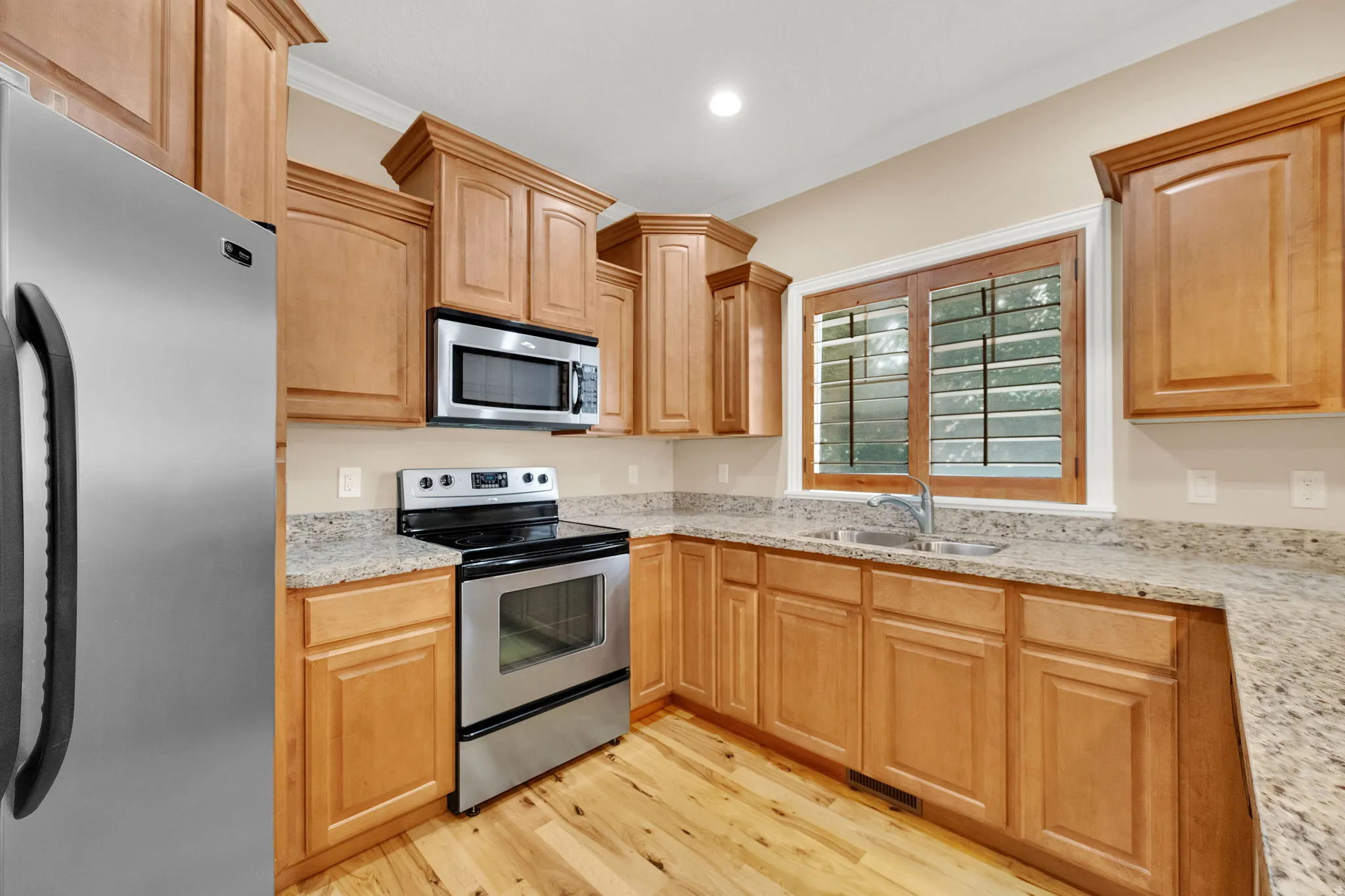 Kitchen featuring light wood-finish cabinetry, granite countertops, stainless steel appliances, and wood-finish flooring