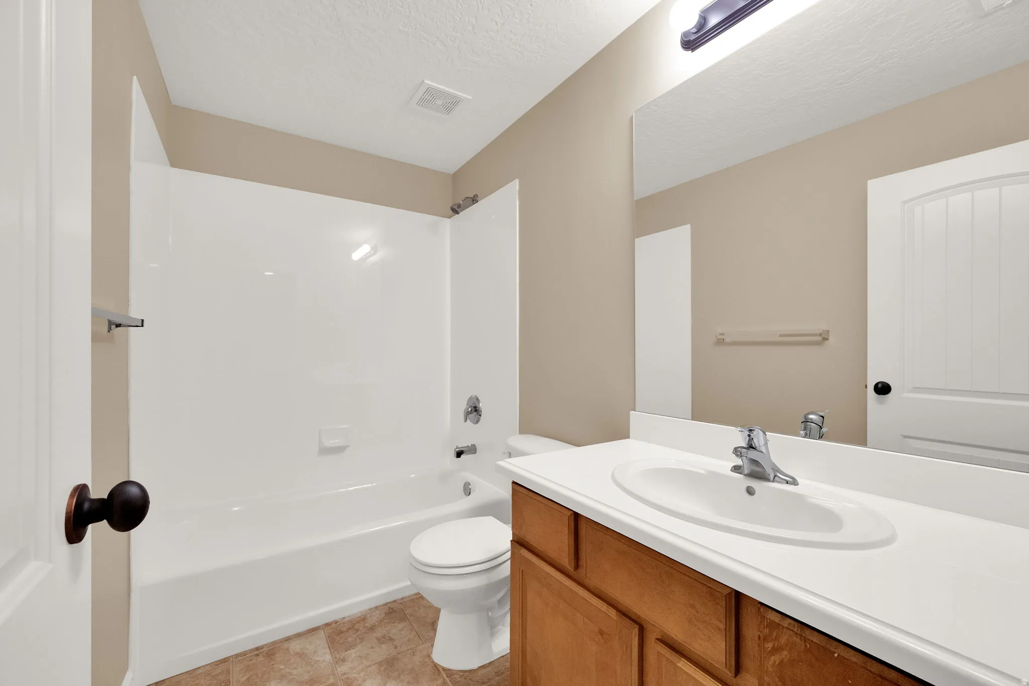 Bathroom featuring a bathtub with an integrated shower, a vanity with a white countertop and oval sink, and a large wall-mounted mirror