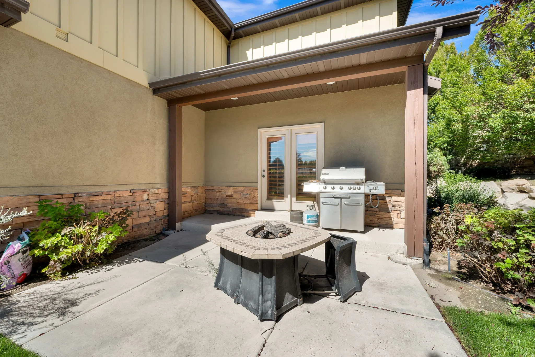 Covered patio with a stone fire pit, textured stucco exterior, and stone veneer accents