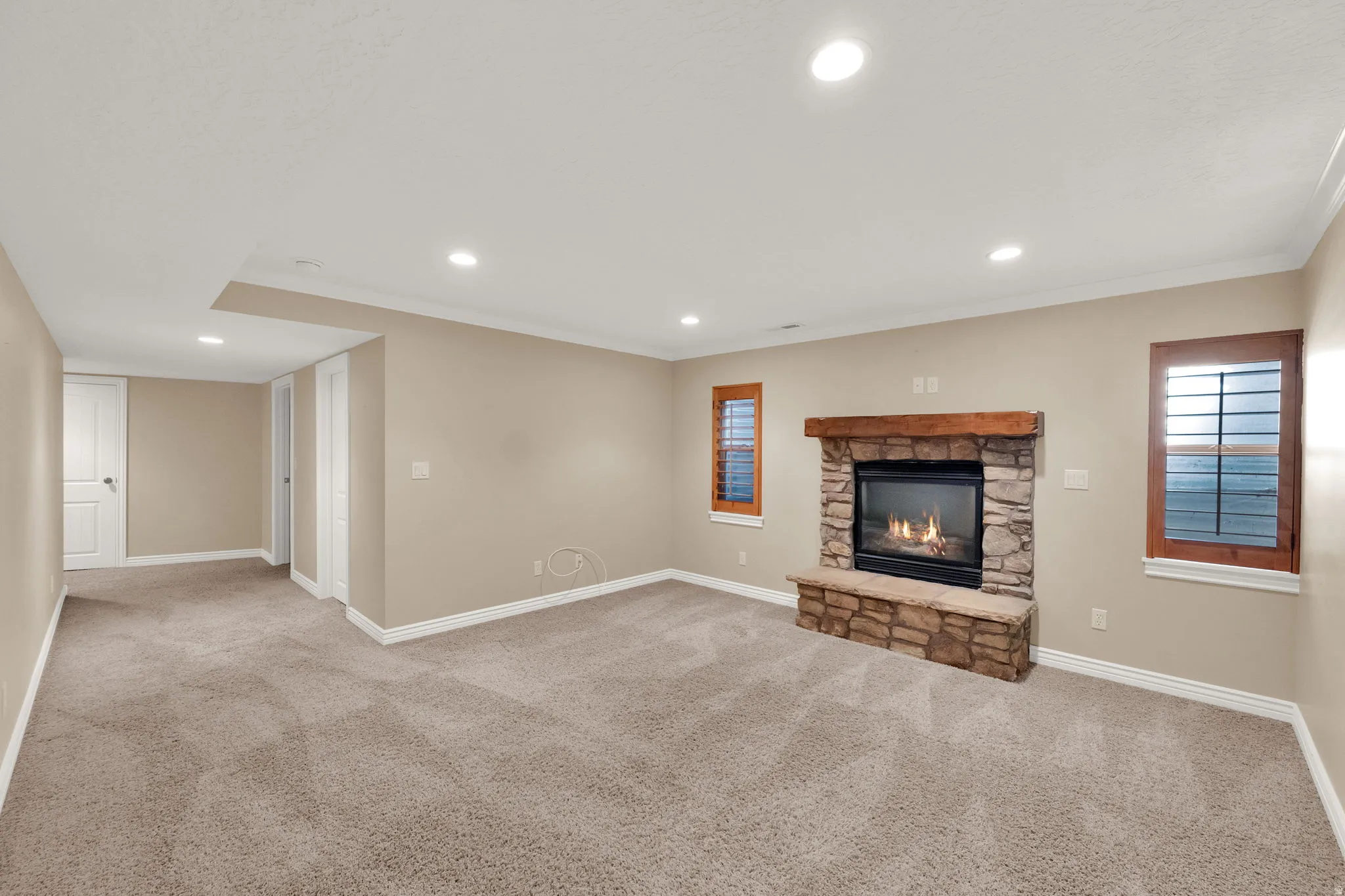 Spacious room featuring a stone fireplace with a wood mantle, recessed lighting, carpet flooring, and window shutters