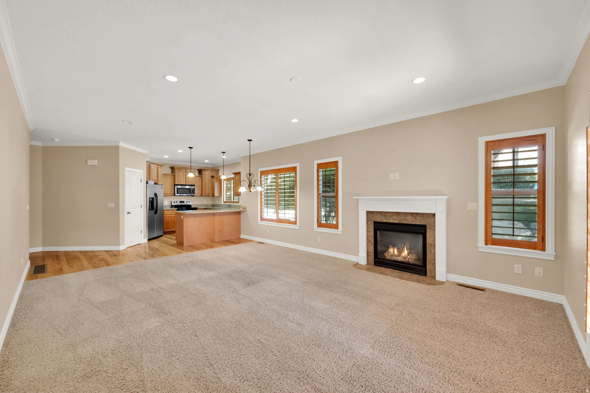Open-concept living space featuring a fireplace with a stone surround, wood-finish flooring, recessed lighting, and a kitchen with wood cabinetry