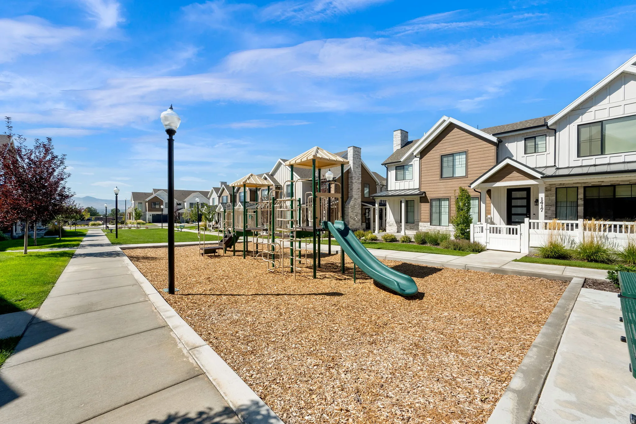 Community playground featuring a slide and climbing structures, bordered by a concrete pathway and green space