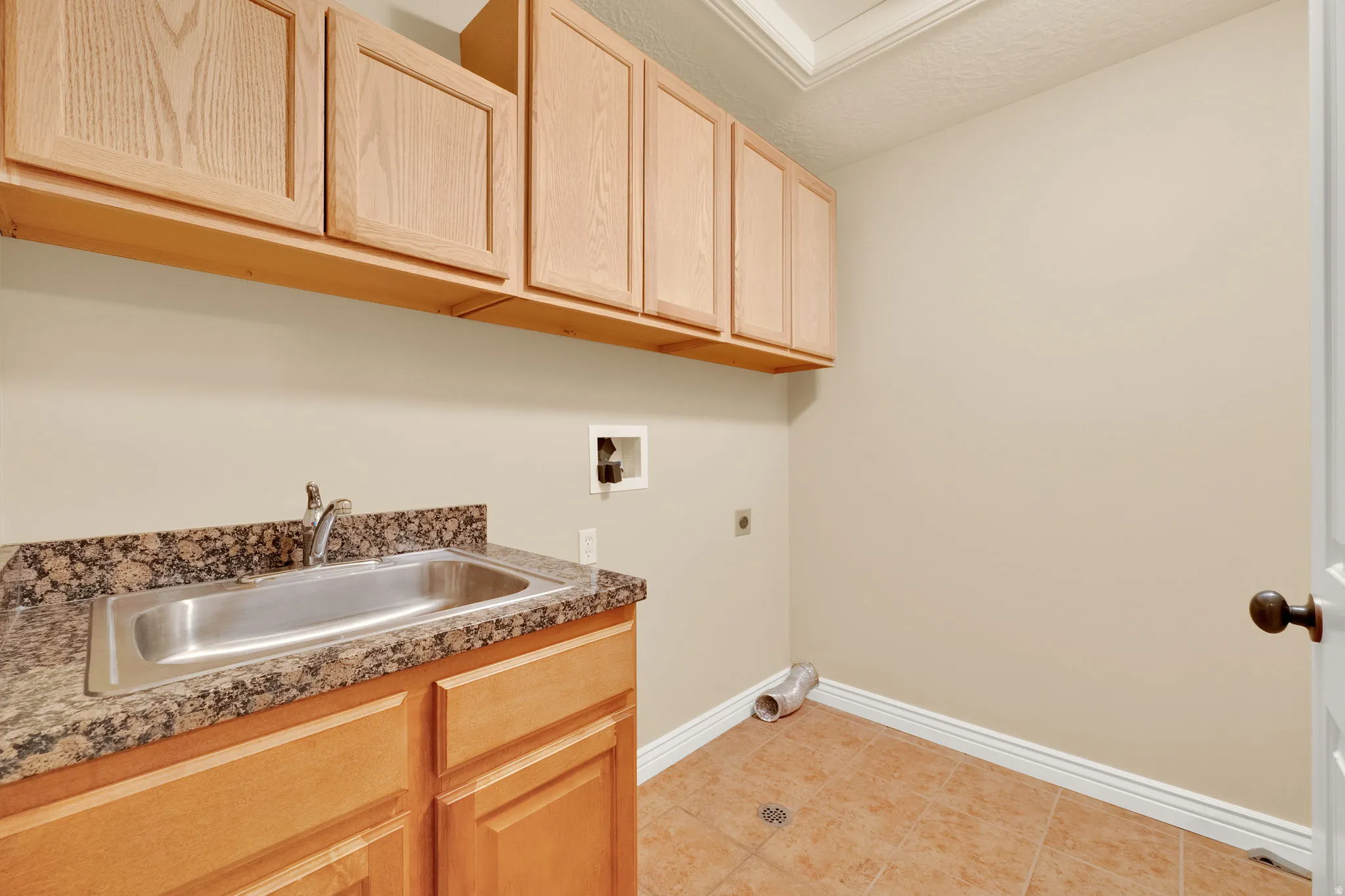 Maple cabinetry, granite-finish countertop, stainless steel utility sink, and tile flooring