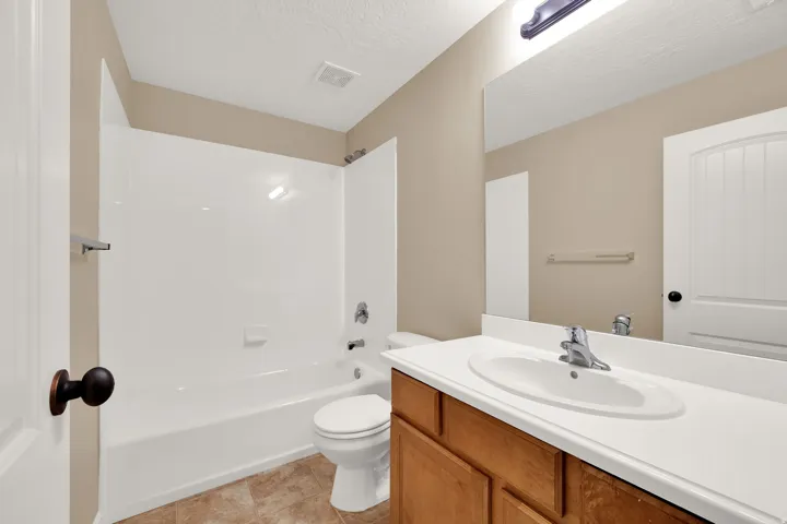 Bathroom featuring a bathtub with an integrated shower, a vanity with a white countertop and oval sink, and a large wall-mounted mirror