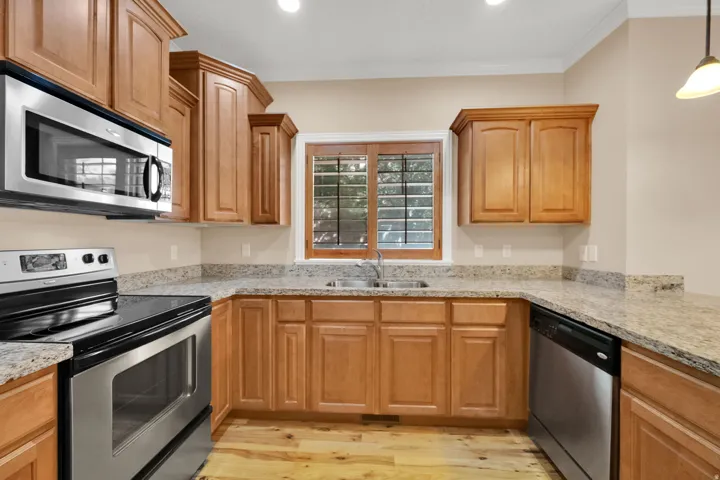 Kitchen featuring stainless steel appliances, wood-finish cabinetry, stone countertops, and wood-finish flooring