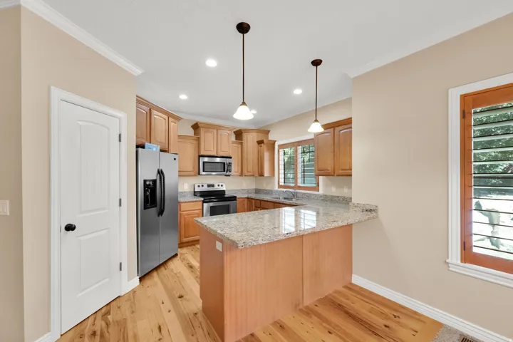Kitchen featuring wood-finish flooring, recessed lighting, pendant lighting, stainless steel appliances, and light wood cabinetry