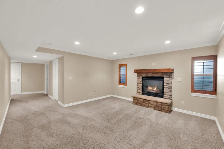 Spacious room featuring a stone fireplace with a wood mantle, recessed lighting, carpet flooring, and window shutters