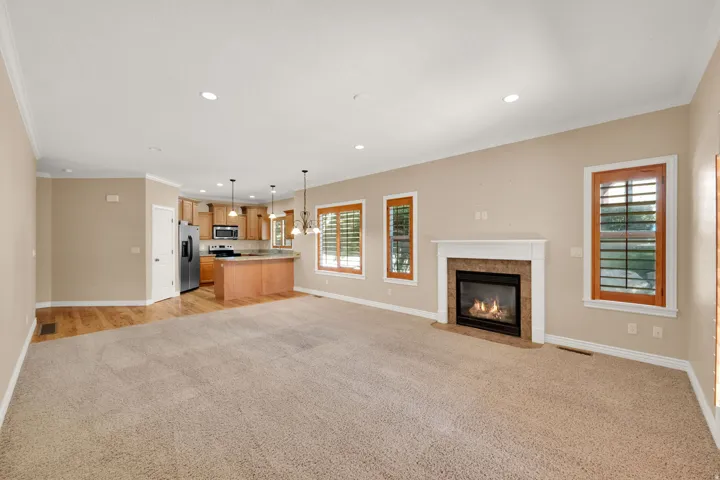 Open-concept living space featuring a fireplace with a stone surround, wood-finish flooring, recessed lighting, and a kitchen with wood cabinetry