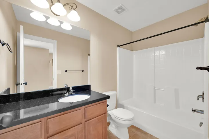 Vanity with a black stone countertop, integrated sink, and wood-finish cabinetry