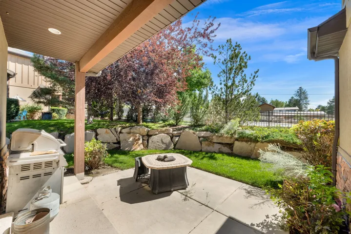 Covered patio with recessed lighting, concrete flooring, stone retaining wall, and landscaped planting beds
