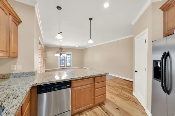 Kitchen featuring granite countertops, wood cabinetry, stainless steel dishwasher, and wood-finish flooring