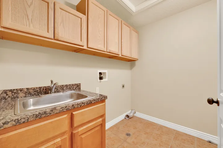 Maple cabinetry, granite-finish countertop, stainless steel utility sink, and tile flooring