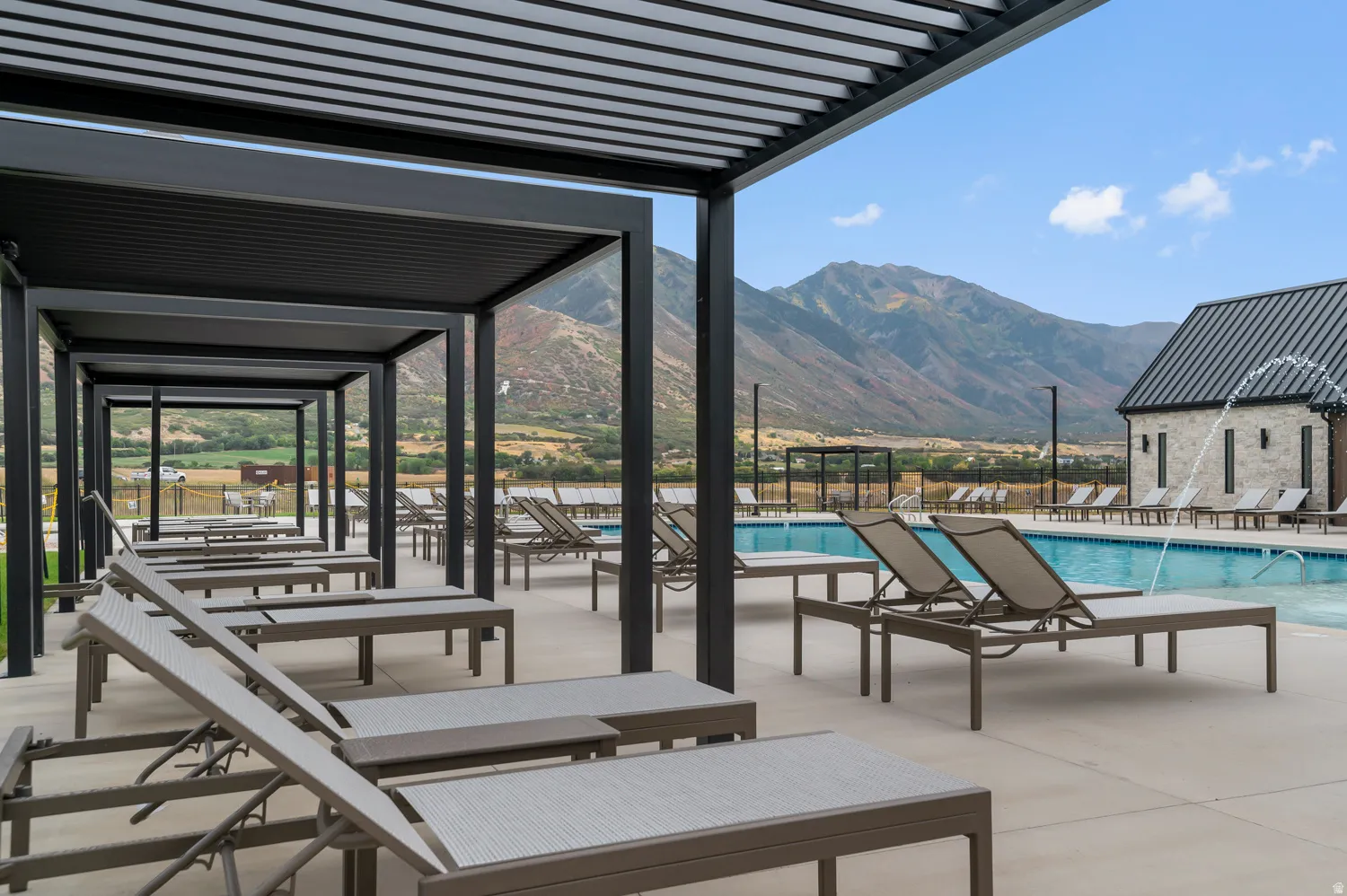 Expansive pool area with a water feature, surrounding lounge seating, and a shaded pergola structure